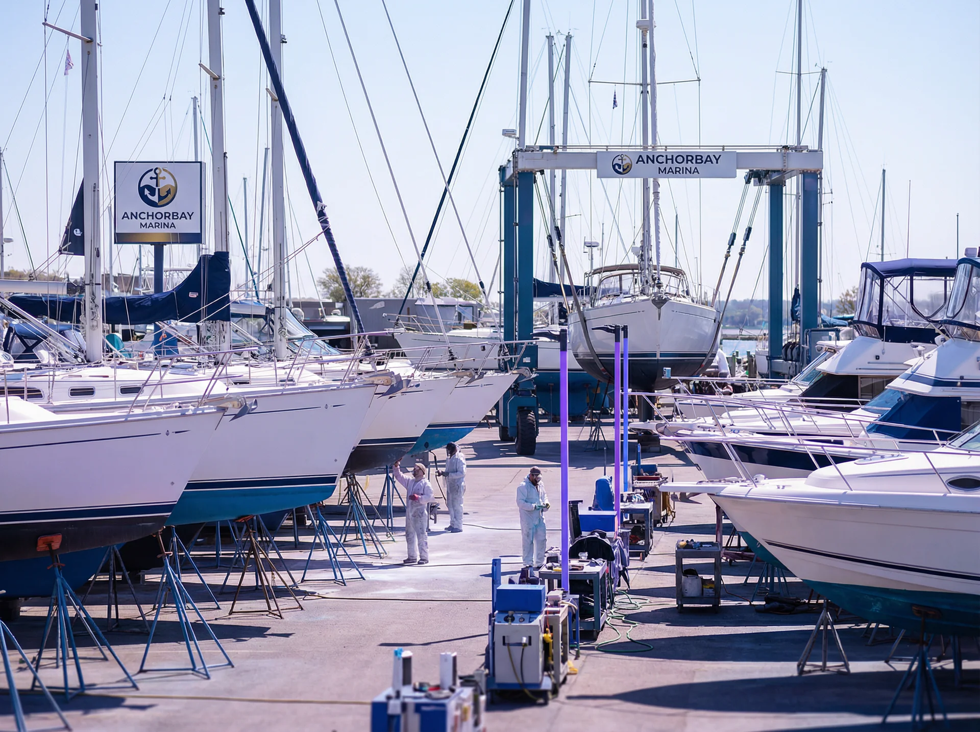 Boats lined up in a marina boatyard ready for spring launch with a travel lift in the background